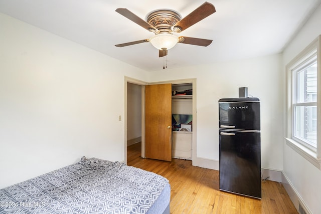 bedroom featuring light wood-type flooring, a closet, black fridge, and ceiling fan