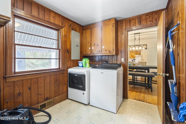 clothes washing area featuring cabinets, separate washer and dryer, electric panel, wood walls, and light hardwood / wood-style floors