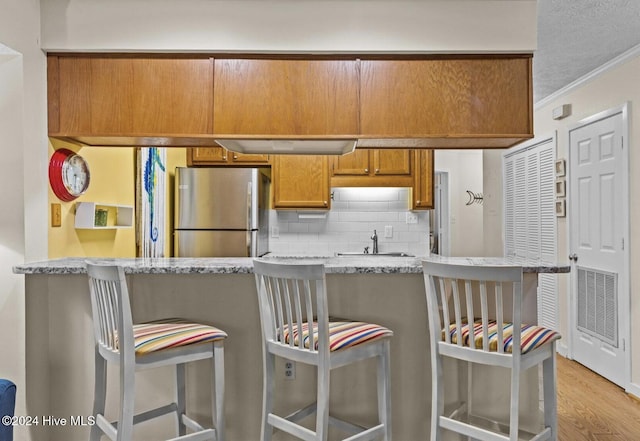 kitchen with stainless steel refrigerator, a kitchen breakfast bar, kitchen peninsula, crown molding, and decorative backsplash