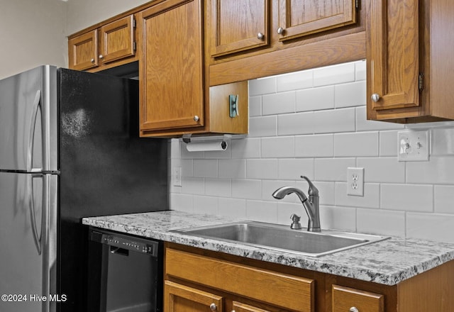 kitchen with dishwasher, sink, light stone counters, backsplash, and stainless steel fridge