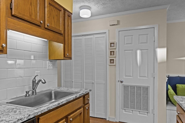 kitchen with sink, decorative backsplash, light stone countertops, a textured ceiling, and ornamental molding