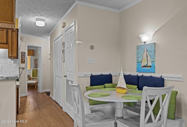 dining space featuring light wood-type flooring, a textured ceiling, breakfast area, and ornamental molding