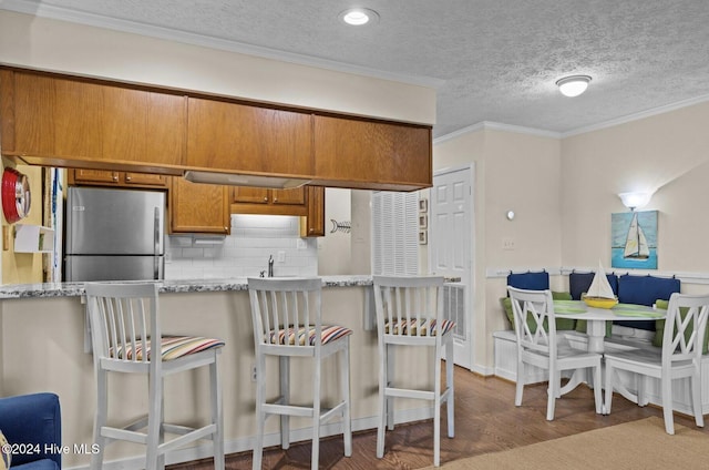 kitchen with stainless steel fridge, backsplash, a textured ceiling, crown molding, and a breakfast bar area