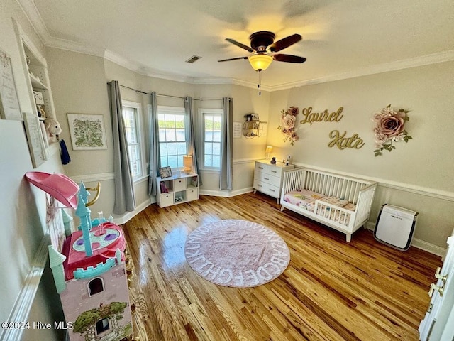 bedroom featuring ceiling fan, light hardwood / wood-style floors, a crib, and crown molding