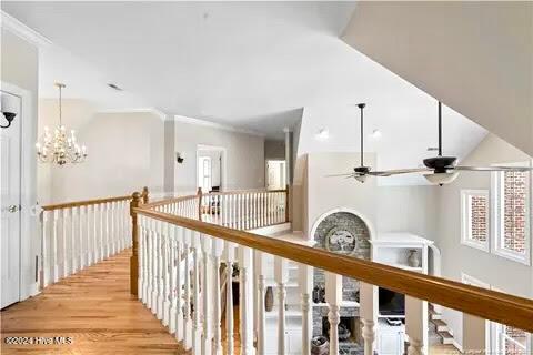 corridor featuring light wood-type flooring, ornamental molding, and an inviting chandelier