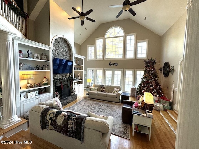 living room featuring a high end fireplace, ornate columns, ceiling fan, hardwood / wood-style flooring, and high vaulted ceiling