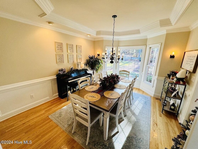 dining room featuring a notable chandelier, light hardwood / wood-style floors, a raised ceiling, and ornamental molding