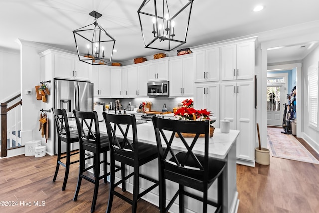 kitchen featuring white cabinetry, stainless steel appliances, a breakfast bar, a center island with sink, and light wood-type flooring