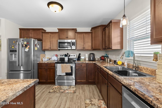 kitchen featuring appliances with stainless steel finishes, decorative light fixtures, light hardwood / wood-style flooring, and sink