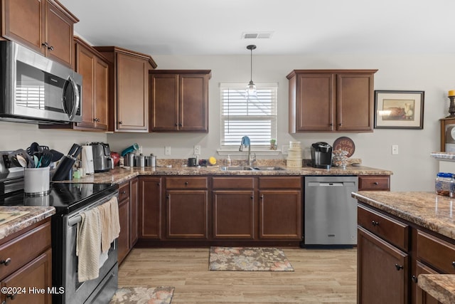 kitchen featuring pendant lighting, sink, light wood-type flooring, light stone counters, and stainless steel appliances