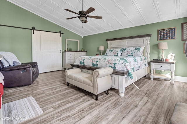 bedroom featuring lofted ceiling, crown molding, ceiling fan, a barn door, and light wood-type flooring