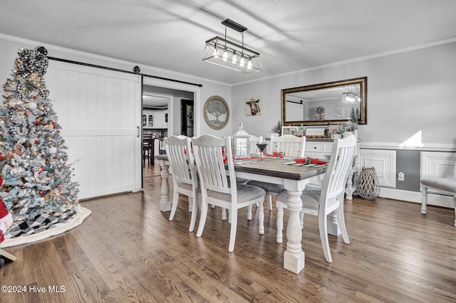 dining area with a barn door, ornamental molding, and hardwood / wood-style flooring