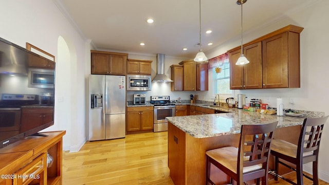 kitchen with wall chimney range hood, kitchen peninsula, light hardwood / wood-style floors, pendant lighting, and appliances with stainless steel finishes