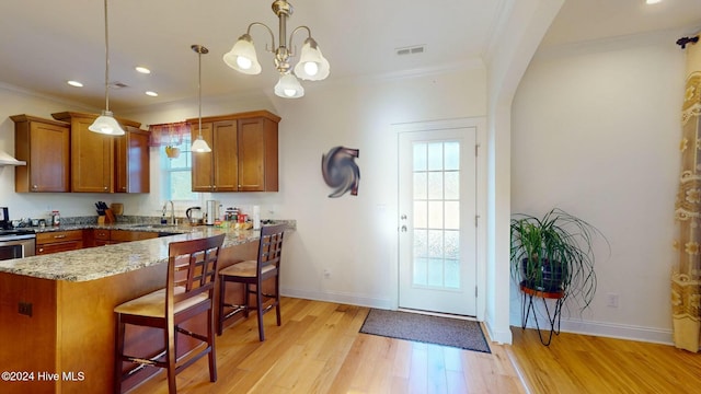 kitchen featuring a kitchen bar, sink, hanging light fixtures, light hardwood / wood-style floors, and light stone counters