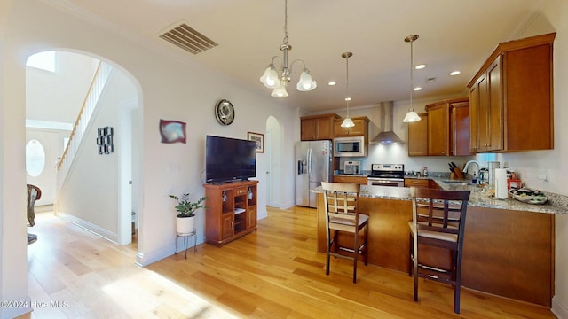 kitchen featuring light wood-type flooring, stainless steel appliances, wall chimney range hood, pendant lighting, and a kitchen island