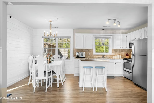 kitchen with white cabinets, pendant lighting, light wood-type flooring, and appliances with stainless steel finishes