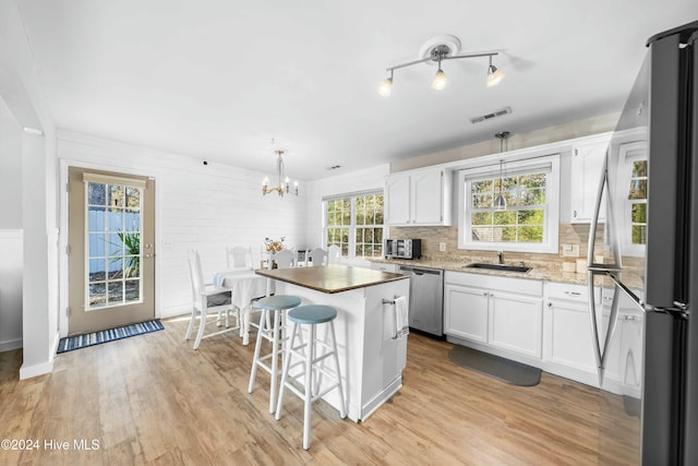 kitchen featuring appliances with stainless steel finishes, decorative light fixtures, light hardwood / wood-style flooring, white cabinets, and a center island