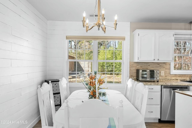 dining room featuring wooden walls, dark hardwood / wood-style flooring, a healthy amount of sunlight, and a notable chandelier