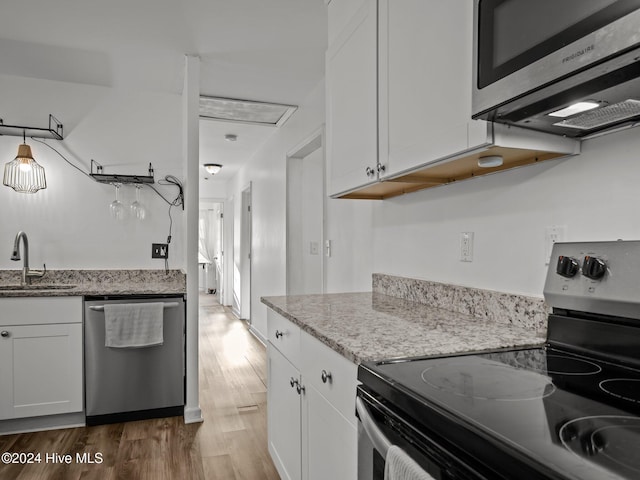 kitchen featuring sink, hardwood / wood-style flooring, light stone countertops, appliances with stainless steel finishes, and white cabinetry