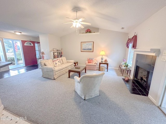 carpeted living room featuring ceiling fan, a fireplace, vaulted ceiling, and a textured ceiling