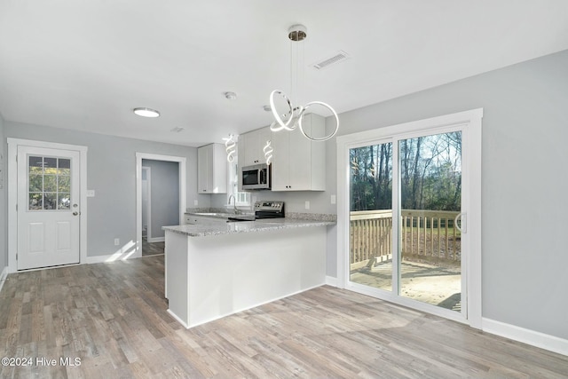 kitchen with a healthy amount of sunlight, stainless steel appliances, kitchen peninsula, decorative light fixtures, and white cabinets