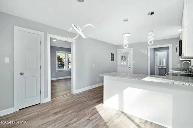 kitchen with light stone countertops, stove, pendant lighting, wood-type flooring, and white cabinetry