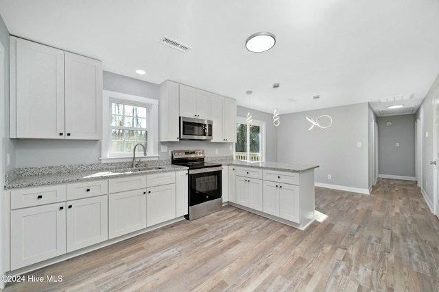 kitchen featuring kitchen peninsula, appliances with stainless steel finishes, pendant lighting, white cabinets, and light wood-type flooring