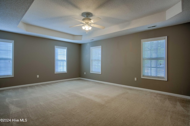 carpeted spare room with a textured ceiling, a tray ceiling, and ceiling fan