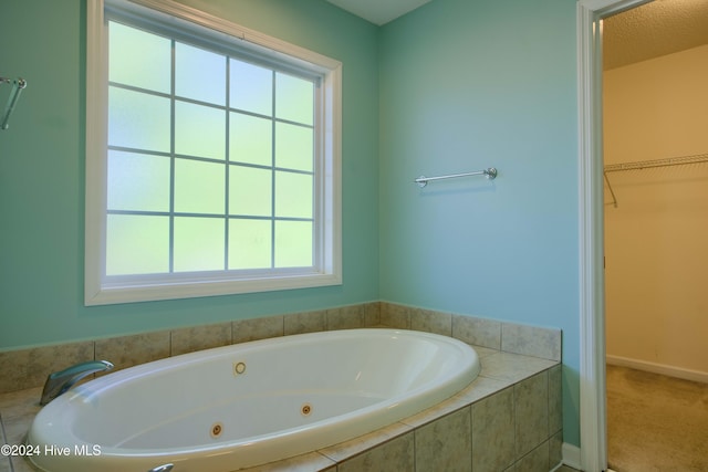 bathroom featuring a relaxing tiled tub, a healthy amount of sunlight, and a textured ceiling