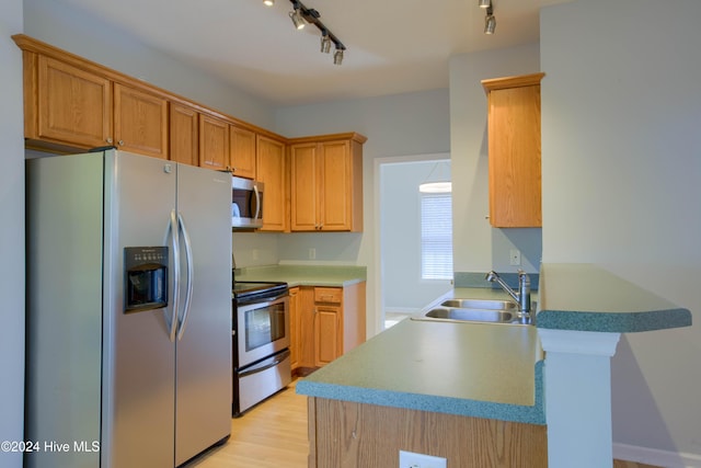 kitchen with kitchen peninsula, appliances with stainless steel finishes, track lighting, sink, and light hardwood / wood-style flooring