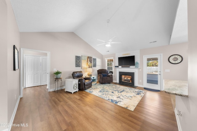 living room featuring ceiling fan, a large fireplace, light hardwood / wood-style floors, and vaulted ceiling