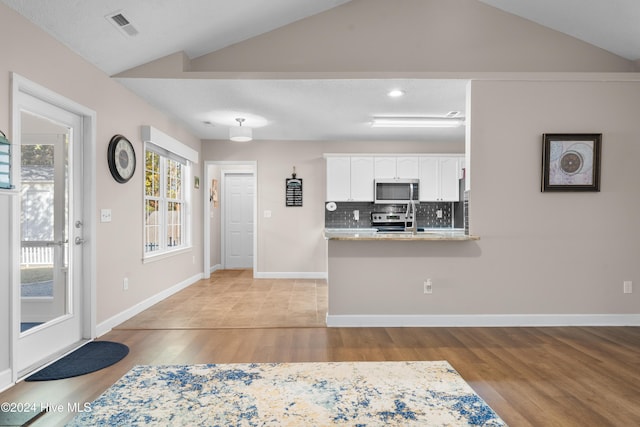 kitchen featuring kitchen peninsula, backsplash, stainless steel appliances, white cabinetry, and lofted ceiling