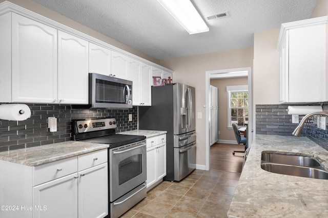 kitchen with appliances with stainless steel finishes, light stone counters, white cabinetry, and sink