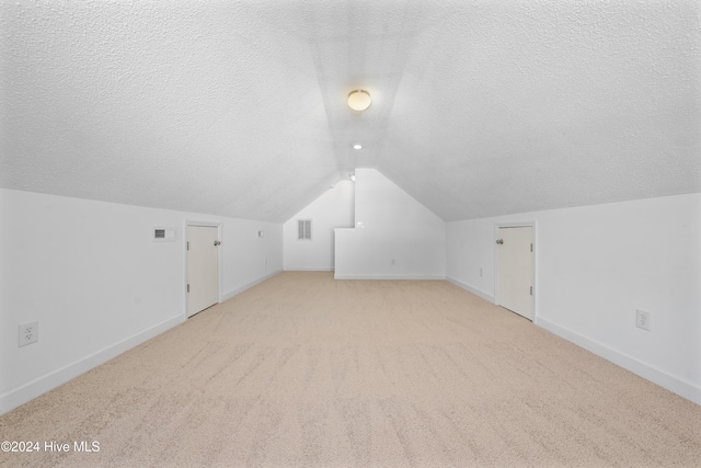 additional living space featuring a textured ceiling, light colored carpet, and lofted ceiling