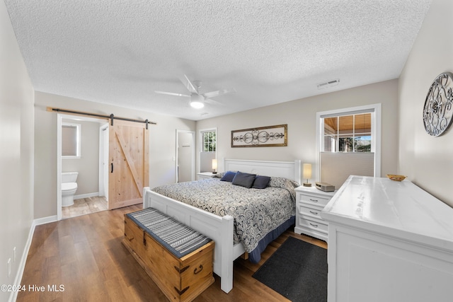 bedroom with a barn door, ensuite bathroom, ceiling fan, and light hardwood / wood-style floors