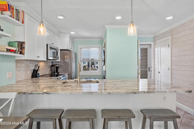 kitchen featuring kitchen peninsula, appliances with stainless steel finishes, pendant lighting, white cabinets, and a breakfast bar area