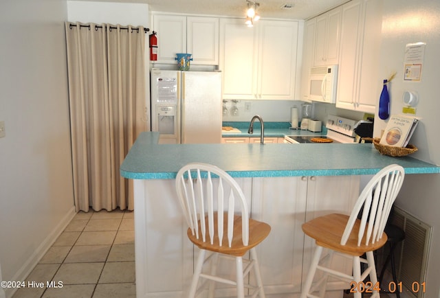 kitchen featuring white appliances, light tile patterned floors, white cabinetry, kitchen peninsula, and a breakfast bar area