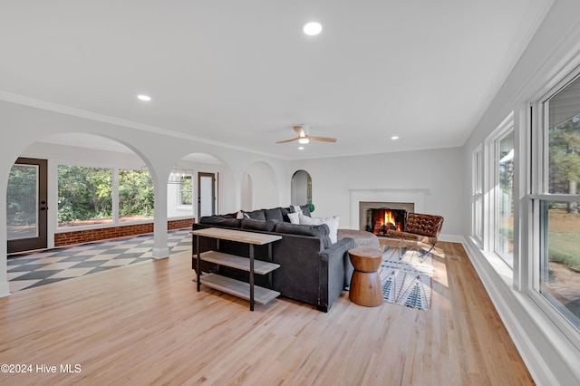 living room with a wealth of natural light, ceiling fan, ornamental molding, and light wood-type flooring