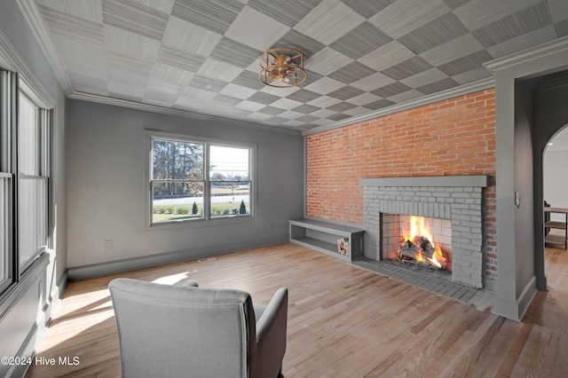 living room with crown molding, a fireplace, light hardwood / wood-style floors, and brick wall