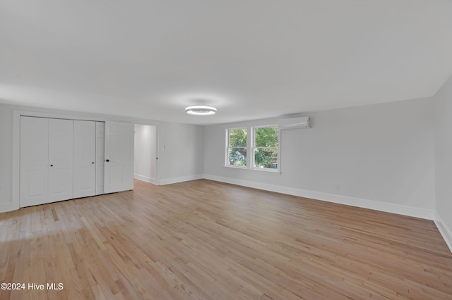 unfurnished bedroom featuring light hardwood / wood-style flooring, a closet, and an AC wall unit