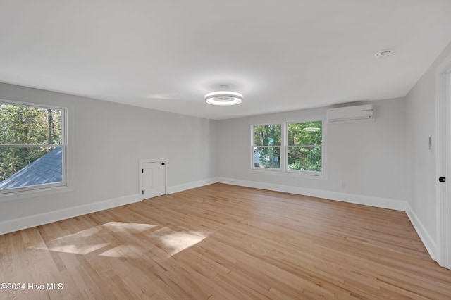 empty room with a healthy amount of sunlight, a wall unit AC, and light hardwood / wood-style flooring