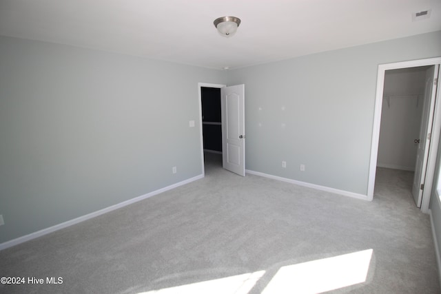 unfurnished bedroom featuring a walk in closet, light carpet, and a closet