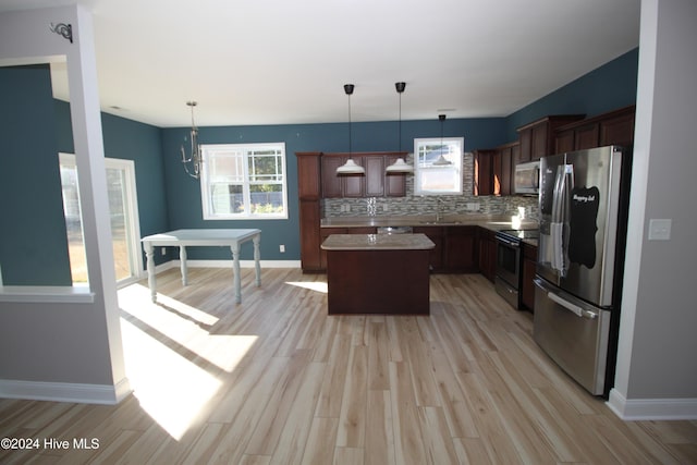 kitchen featuring pendant lighting, light hardwood / wood-style floors, appliances with stainless steel finishes, tasteful backsplash, and a kitchen island