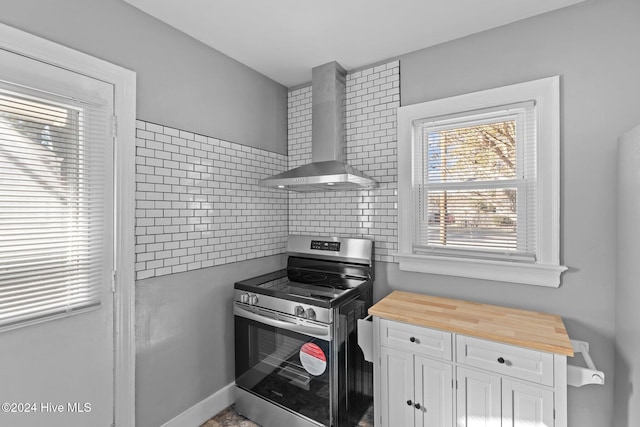 kitchen with wooden counters, tasteful backsplash, wall chimney exhaust hood, stainless steel range oven, and white cabinets