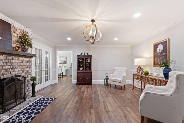 sitting room featuring an inviting chandelier, wood-type flooring, ornamental molding, a brick fireplace, and french doors