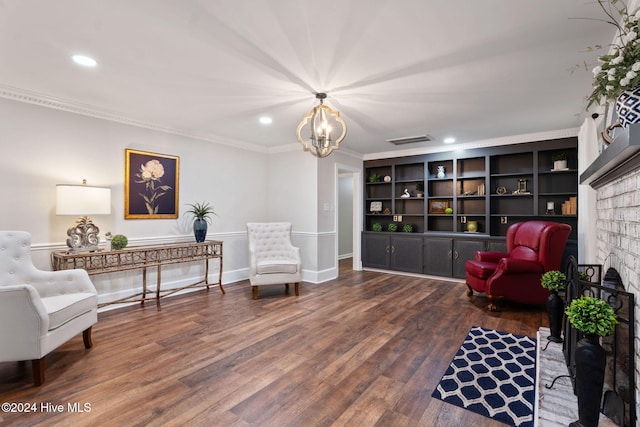 living area with built in features, wood-type flooring, ornamental molding, a brick fireplace, and a chandelier