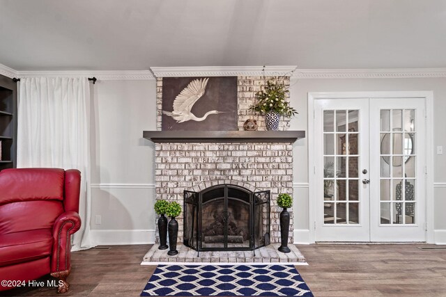 sitting room featuring ornamental molding, a notable chandelier, a brick fireplace, dark wood-type flooring, and french doors