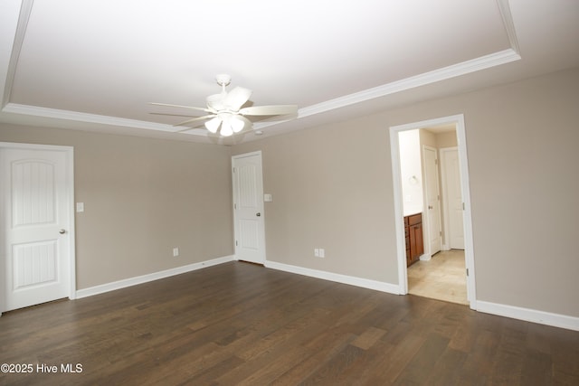 empty room with ceiling fan, crown molding, dark wood-type flooring, and a tray ceiling