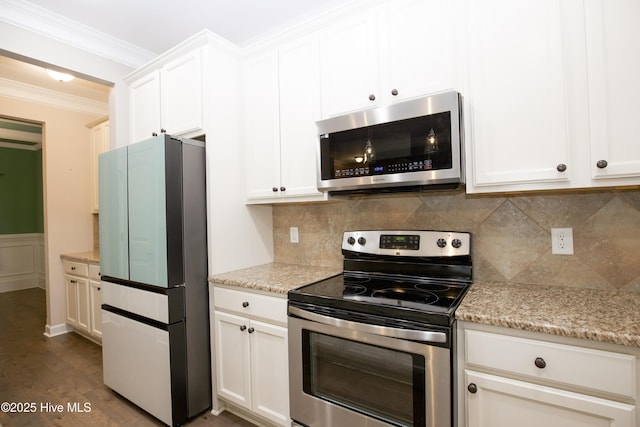 kitchen with ornamental molding, appliances with stainless steel finishes, white cabinetry, light stone counters, and wood-type flooring