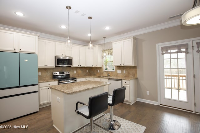 kitchen with sink, hanging light fixtures, stainless steel appliances, a kitchen island, and white cabinets